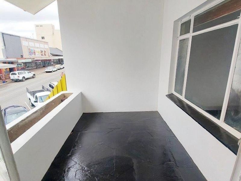 A clean, covered balcony featuring dark stone-look flooring and a large window, offering an elevated view of the street below.