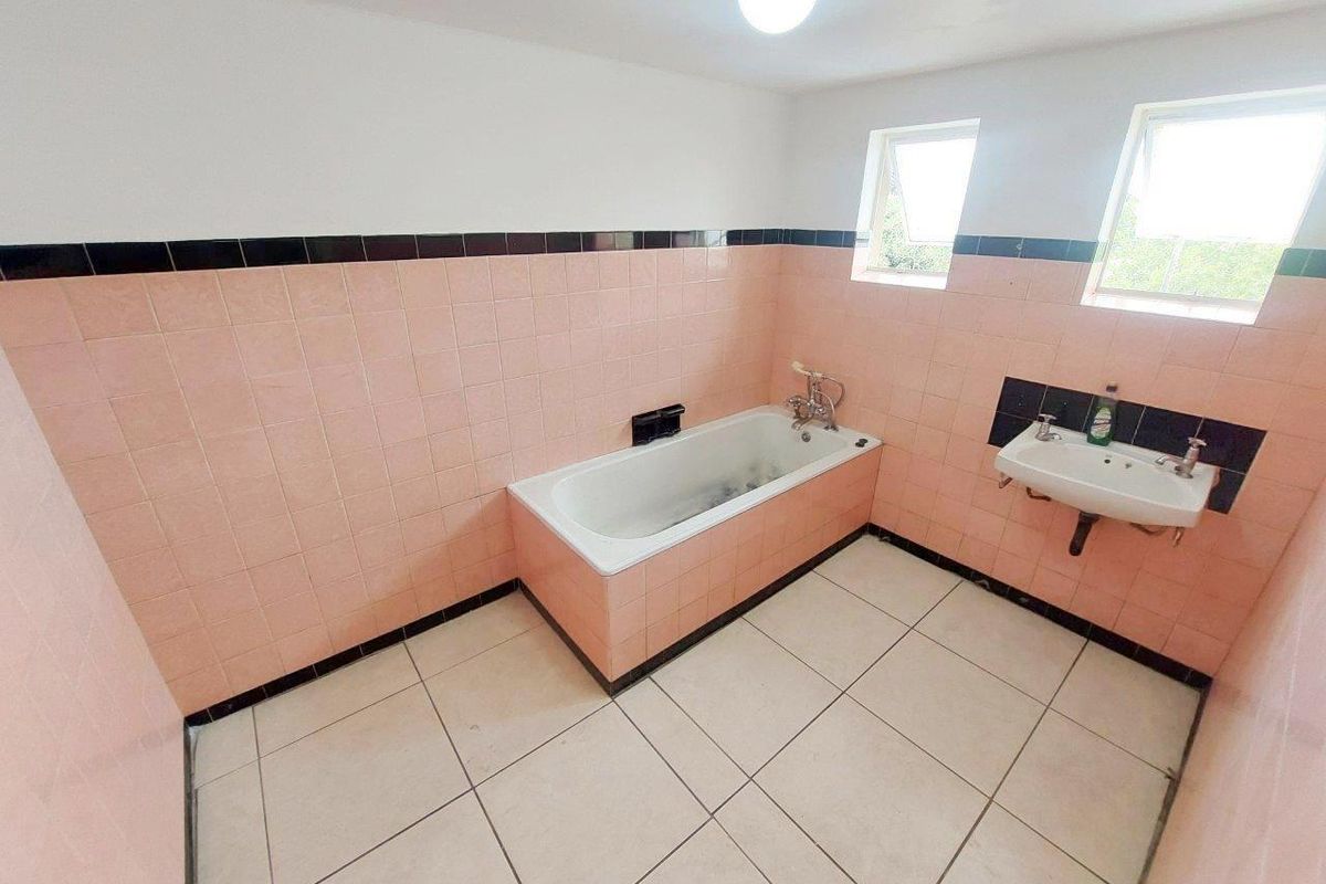 A spacious, empty bathroom featuring a built-in bathtub, wall-mounted basin, and dated pink and black ceramic tiling throughout.
