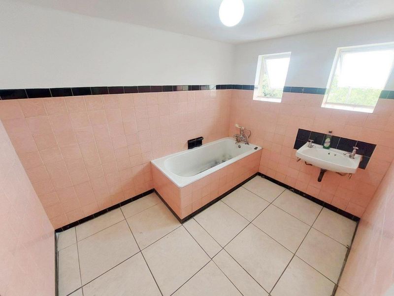 A spacious, empty bathroom featuring a built-in bathtub, wall-mounted basin, and dated pink and black ceramic tiling throughout.