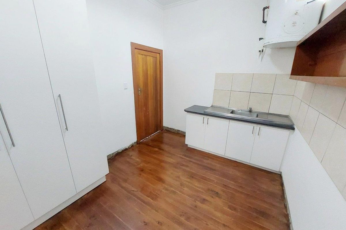 A compact kitchen area featuring white built-in cabinetry, a stainless steel sink, tiled splashback, and timber flooring, currently awaiting final finishing touches.