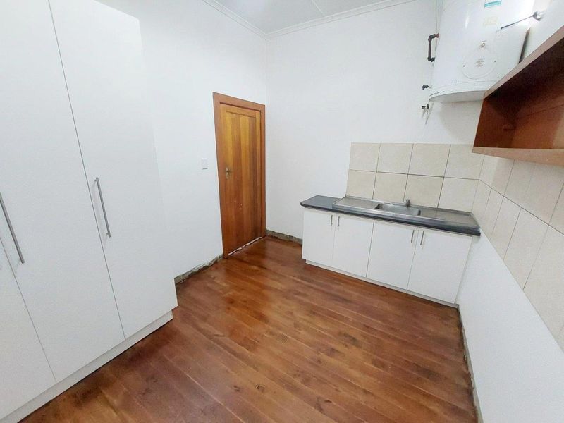 A compact kitchen area featuring white built-in cabinetry, a stainless steel sink, tiled splashback, and timber flooring, currently awaiting final finishing touches.