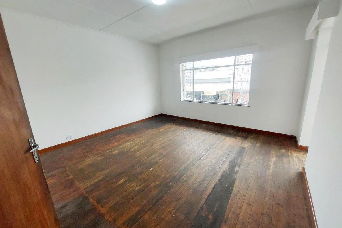 An empty bedroom featuring original timber flooring, neutral walls, and a large window providing natural light.