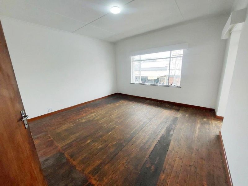 An empty bedroom featuring original timber flooring, neutral walls, and a large window providing natural light.