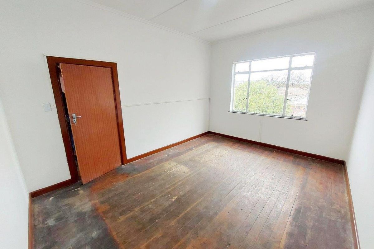 An empty bedroom featuring original timber flooring, white walls, and a large window providing natural light.