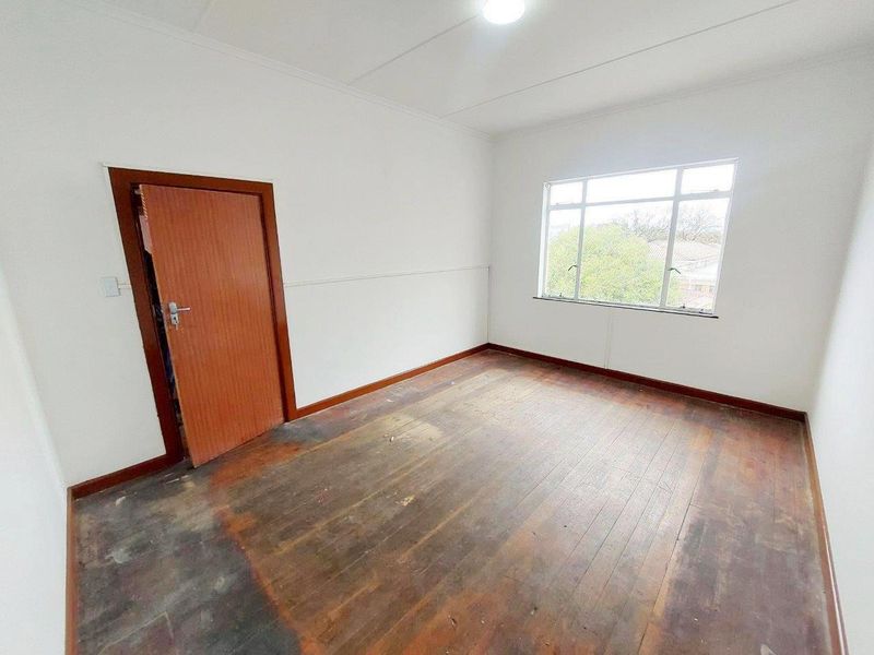 An empty bedroom featuring original timber flooring, white walls, and a large window providing natural light.