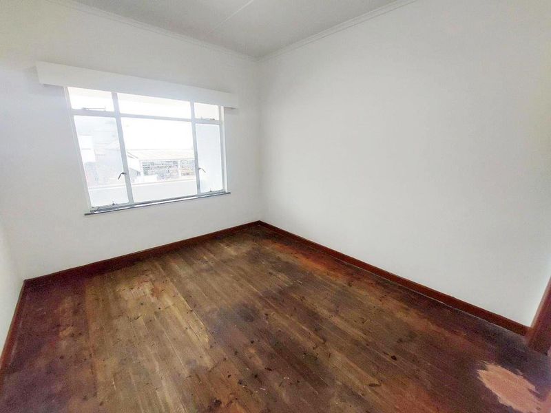 An empty bedroom featuring original timber flooring and a large window, providing a blank canvas for renovation or interior design updates.