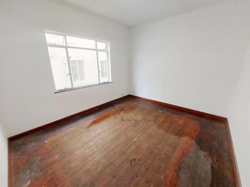 An empty bedroom featuring white walls and original timber flooring that requires refinishing or replacement.