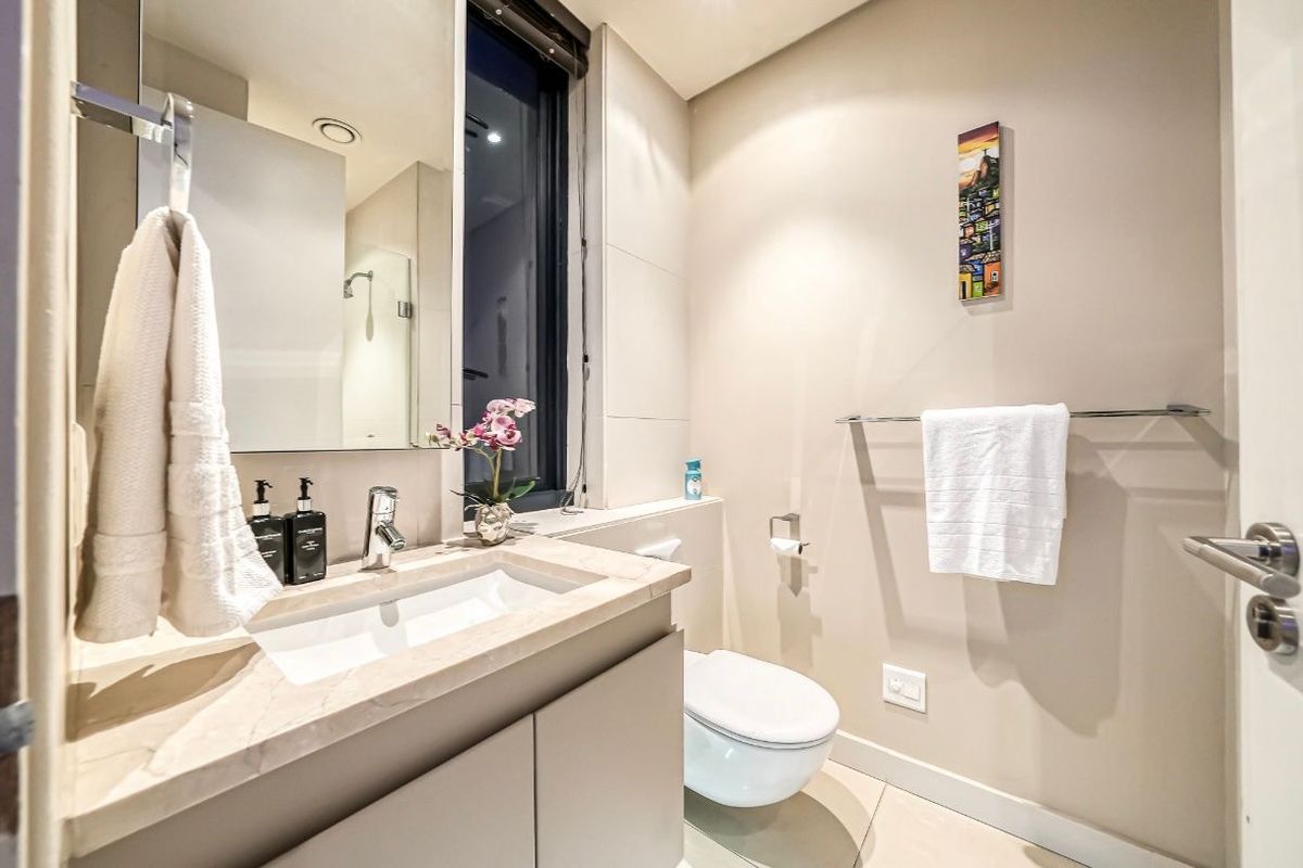 Modern bathroom featuring a stone-topped vanity, wall-mounted toilet, and a large mirror, finished with neutral floor and wall tiles.