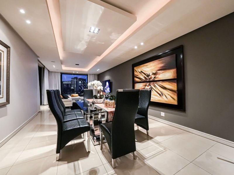 Modern dining area featuring polished floor tiles, a recessed tray ceiling with integrated ambient lighting, and a sleek, contemporary design aesthetic.