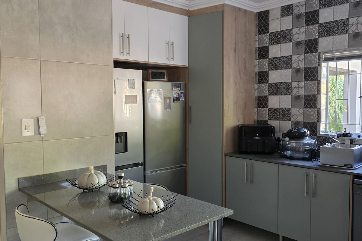 Modern kitchen featuring stone countertops, built-in cabinetry, a breakfast bar, and decorative tiled backsplash with integrated lighting.