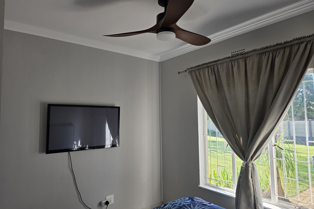 A bedroom featuring a ceiling fan, crown molding, and a window with security bars overlooking the garden.