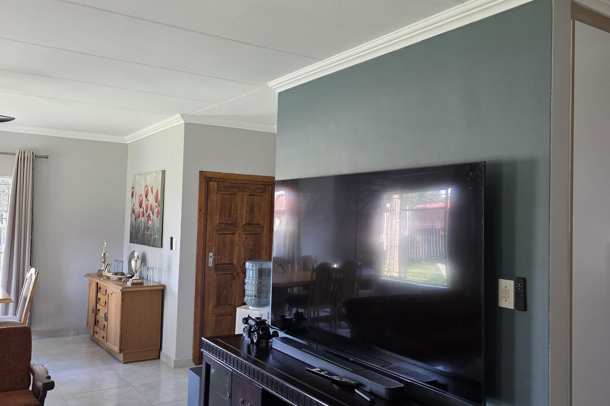 A view of the living area featuring tiled flooring, crown molding, and a feature wall, with an adjacent dining space visible.