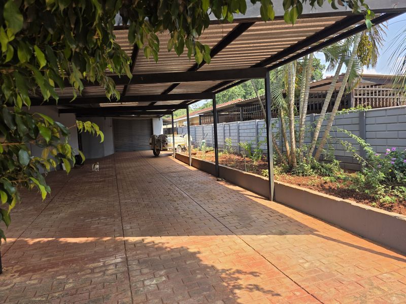 A spacious covered carport featuring brick paving, a sturdy steel structure, and a raised garden bed along the boundary wall.
