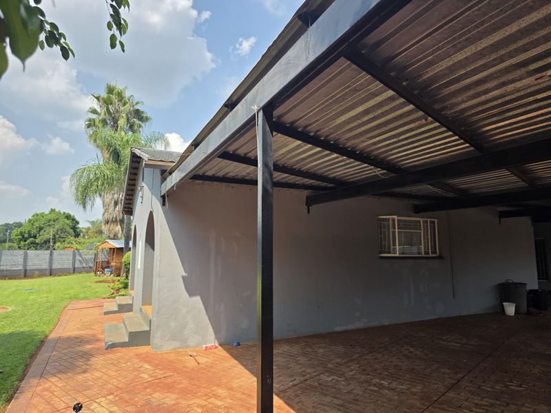 A covered outdoor patio area featuring a corrugated metal roof, steel support structure, and paved flooring, adjacent to the main house exterior.