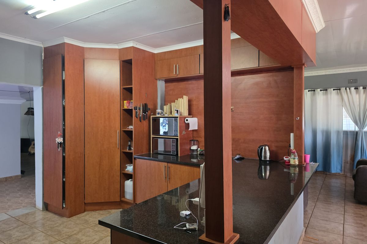 A kitchen featuring dark granite countertops, extensive wooden cabinetry, and a breakfast bar, with tiled flooring and a central structural support pillar.