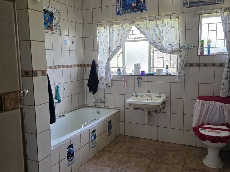 A dated bathroom featuring a built-in bathtub, wall-mounted basin, and toilet, finished with ceramic wall and floor tiles.
