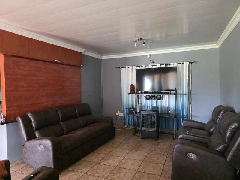 A living room featuring tiled flooring, a panelled ceiling with decorative cornice, and a built-in wooden feature wall.