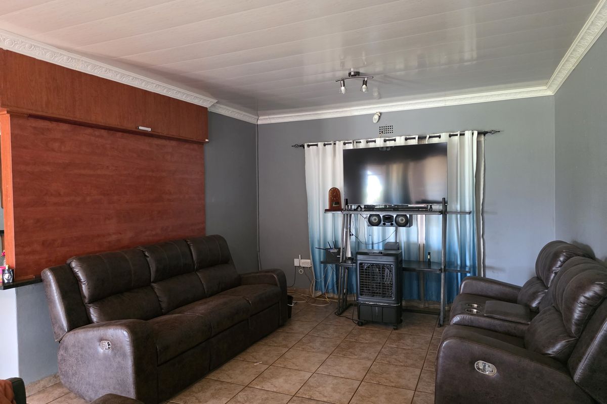 A living room featuring tiled flooring, a panelled ceiling with decorative cornice, and a built-in wooden feature wall.