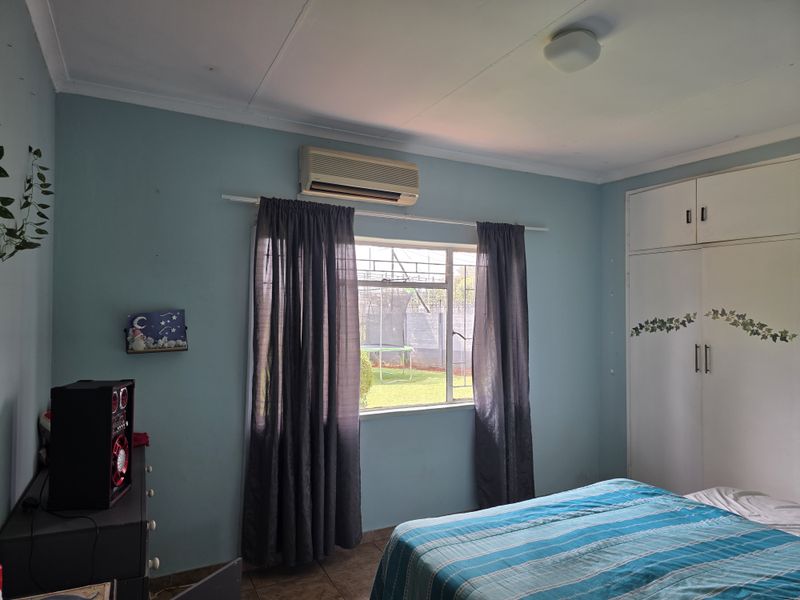 A bedroom featuring built-in cupboards, tiled flooring, and an air conditioning unit, with natural light provided by a window with security bars.