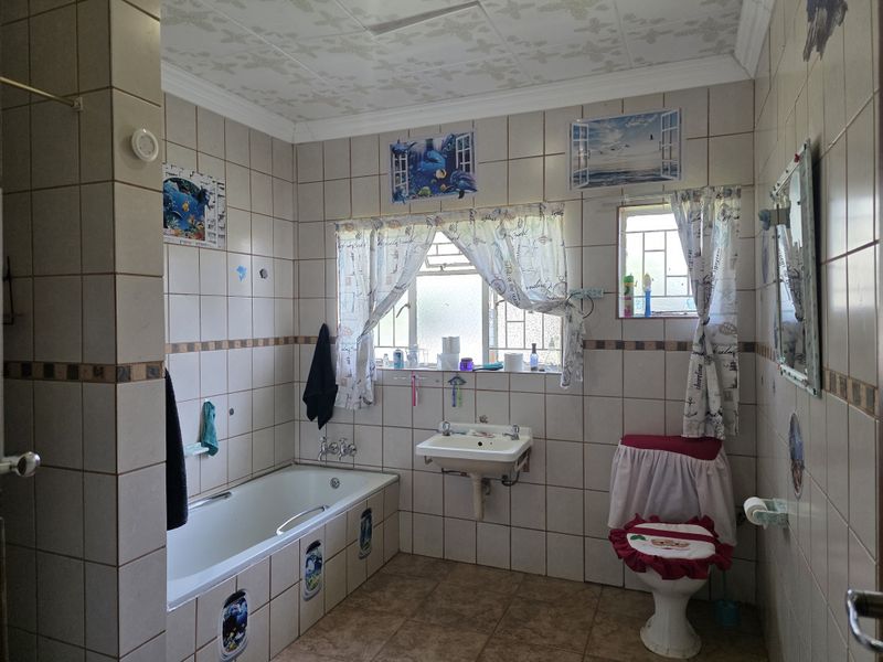 A dated bathroom featuring a built-in bathtub, wall-mounted basin, and toilet, finished with full-height wall tiling and floor tiles.