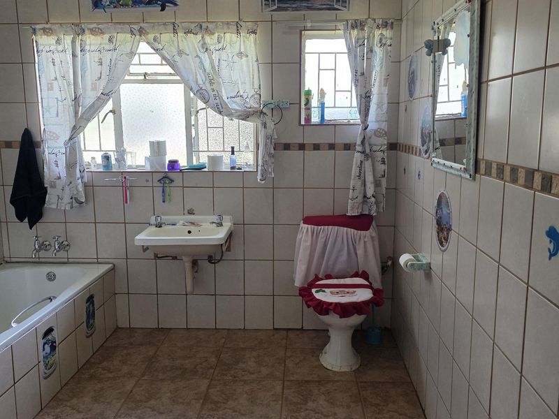 A dated bathroom featuring a bathtub, wall-mounted basin, and toilet, finished with full-height ceramic wall tiling and floor tiles.