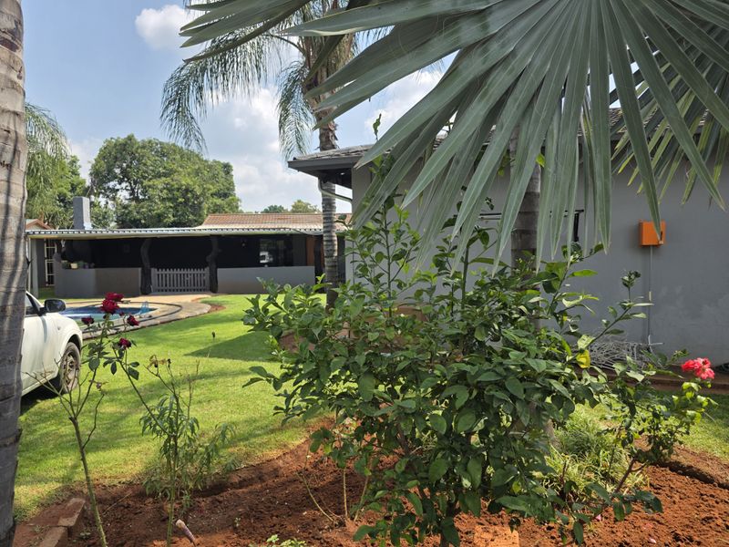 A view of the rear garden featuring a swimming pool, a covered patio area, and established landscaping.