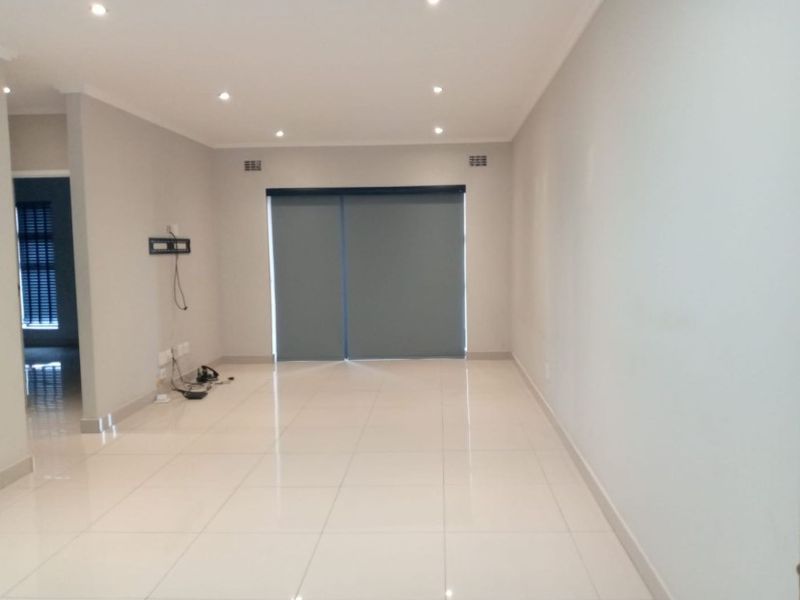 A bright, open-plan living area featuring neutral tiled flooring, recessed downlighting, and large sliding doors with fitted roller blinds.