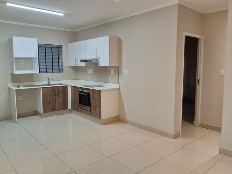 A clean, modern kitchen featuring white upper cabinetry, wood-finish lower cabinets, a built-in oven, hob, extractor fan, and tiled flooring.