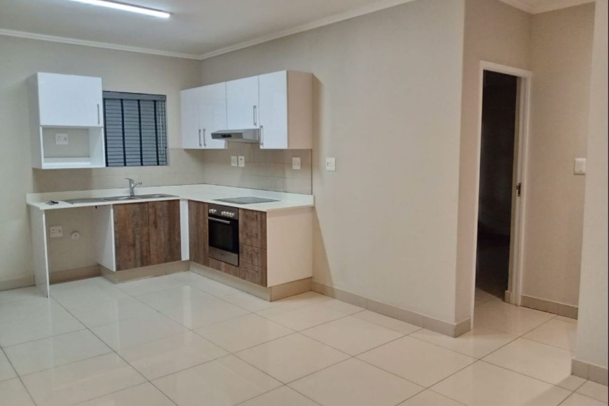A clean, modern kitchen featuring white upper cabinetry, wood-finish lower cabinets, a built-in oven, hob, extractor fan, and tiled flooring.