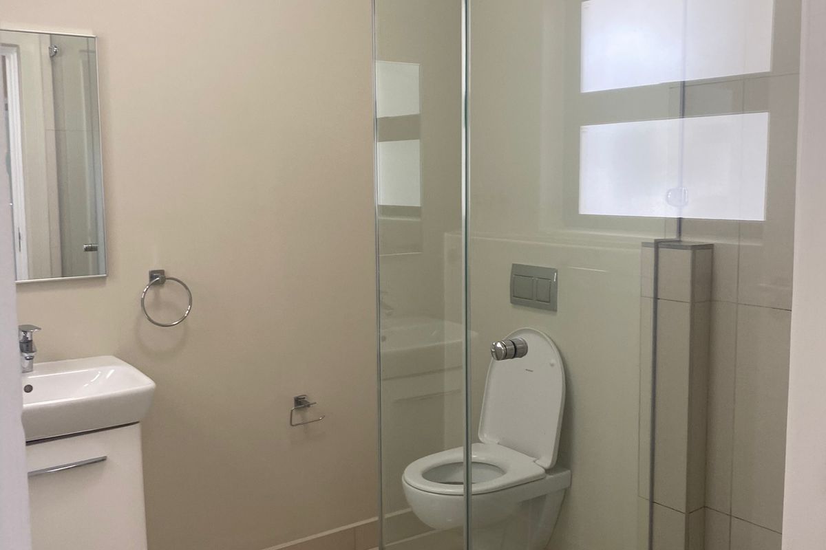 Modern bathroom featuring a glass-enclosed shower, wall-mounted toilet, and a sleek vanity basin with neutral tiling throughout.