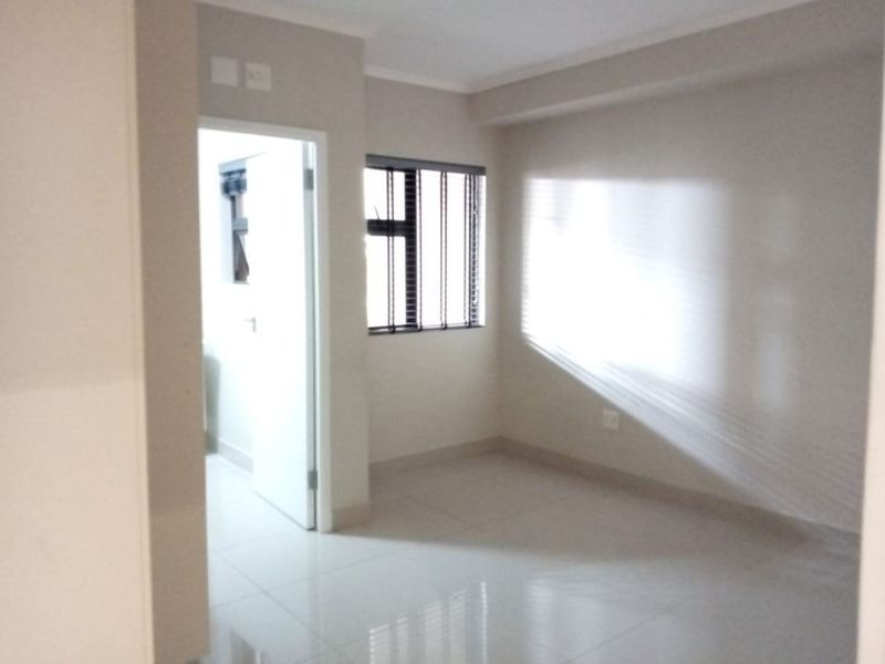 A bright, empty bedroom featuring neutral tiled flooring, clean walls, and a window with fitted blinds, offering a versatile space for personalization.