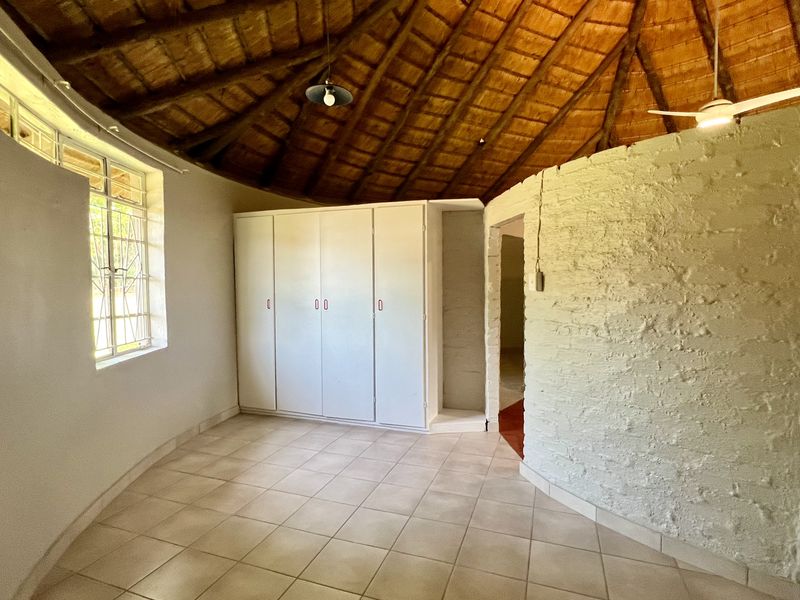 Spacious bedroom featuring a unique circular layout, high thatched ceiling with exposed rafters, built-in cupboards, and tiled flooring.
