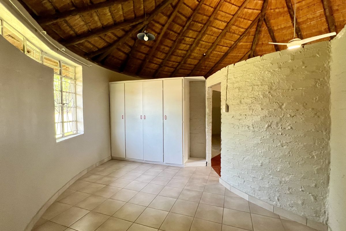 Spacious bedroom featuring a unique circular layout, high thatched ceiling with exposed rafters, built-in cupboards, and tiled flooring.