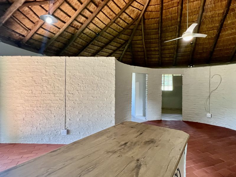 Spacious open-plan living area featuring a traditional thatched roof with exposed timber rafters, terracotta tile flooring, and textured white masonry walls.