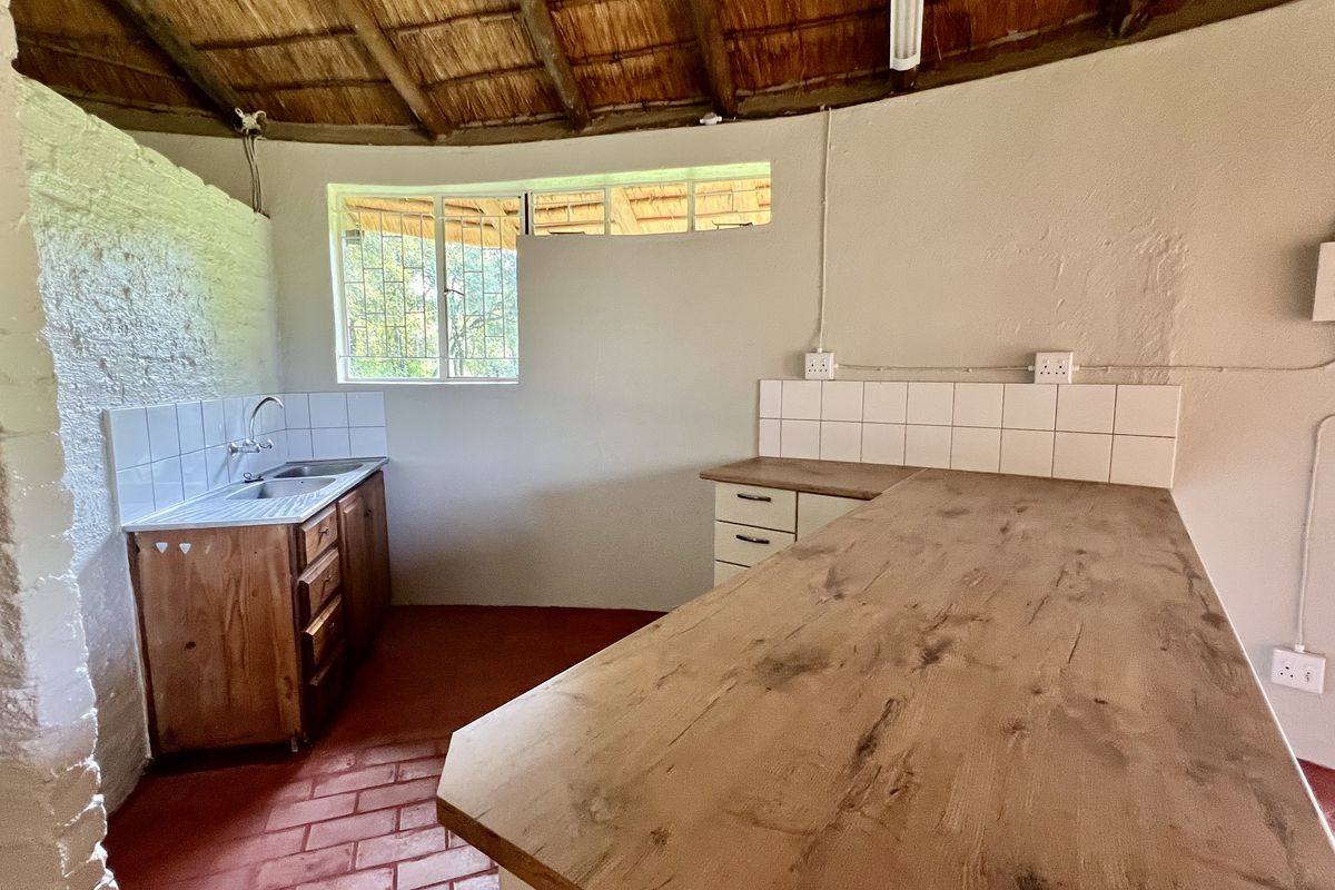 A rustic kitchen area featuring a thatched roof, wooden cabinetry, stainless steel sink, and exposed brick flooring in a circular layout.