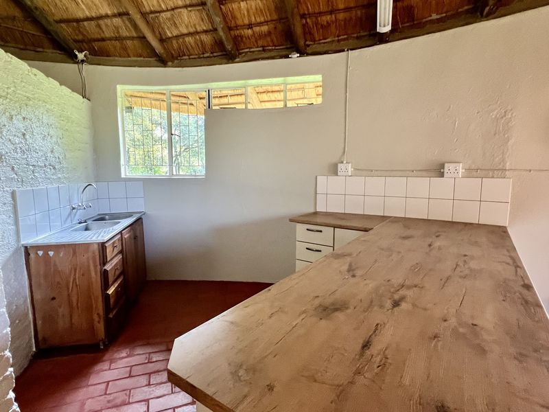 A rustic kitchen area featuring a thatched roof, wooden cabinetry, stainless steel sink, and exposed brick flooring in a circular layout.