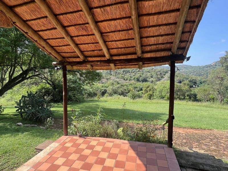 A covered outdoor patio featuring a traditional thatched roof and tiled flooring, offering expansive views of the surrounding garden and natural landscape.