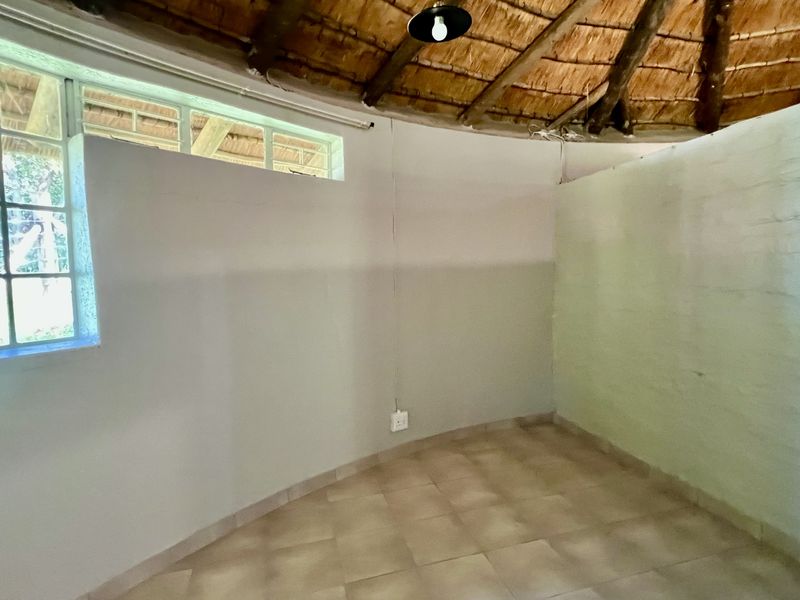 An empty bedroom featuring a traditional thatched roof with exposed timber rafters, tiled flooring, and painted brick walls.