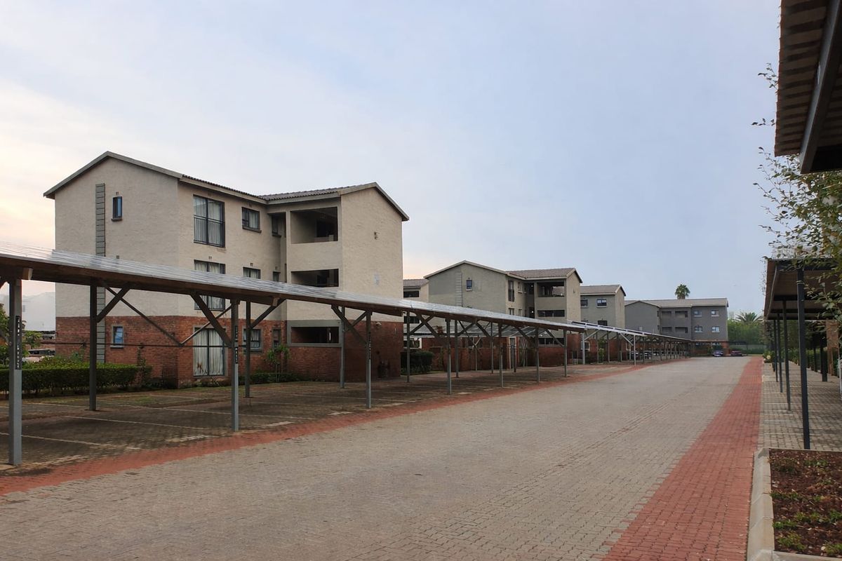 Exterior view of an apartment complex featuring covered parking bays and multi-story residential buildings with brick and plaster facades.