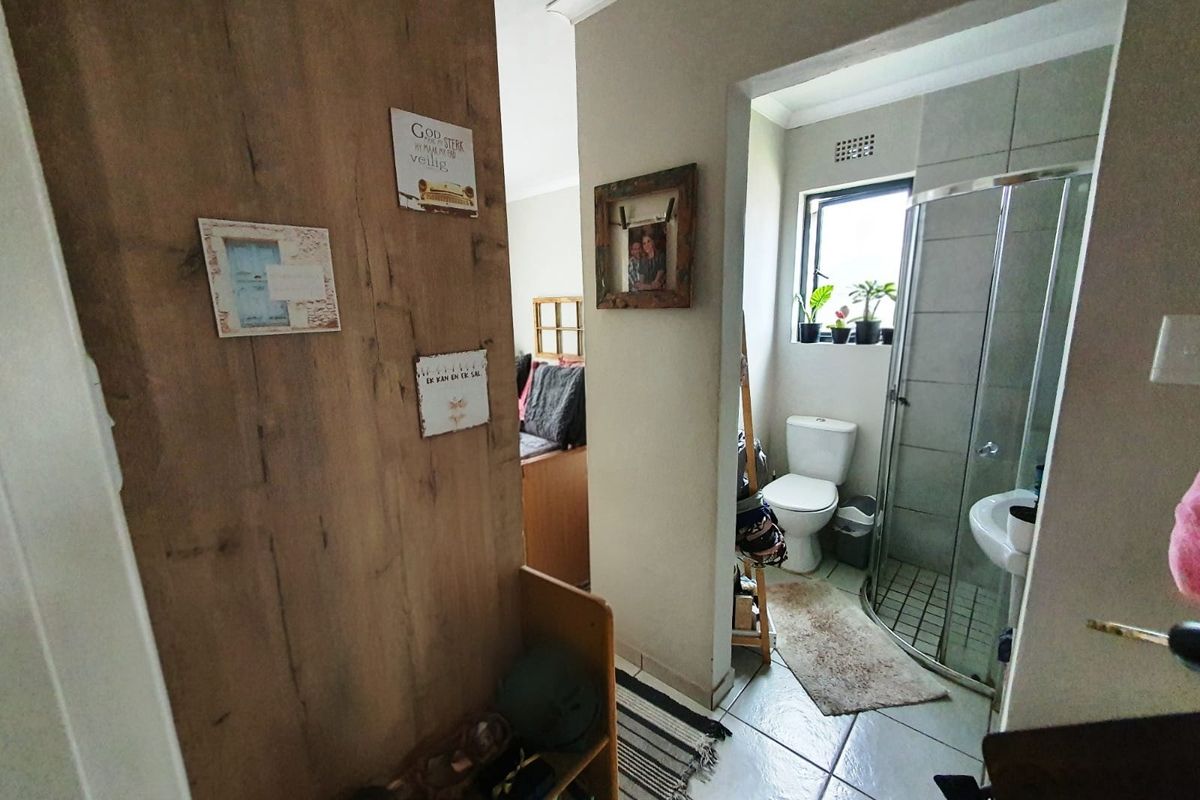 A view into a compact bathroom featuring a corner shower enclosure, pedestal basin, and toilet, with tiled flooring and neutral wall finishes.
