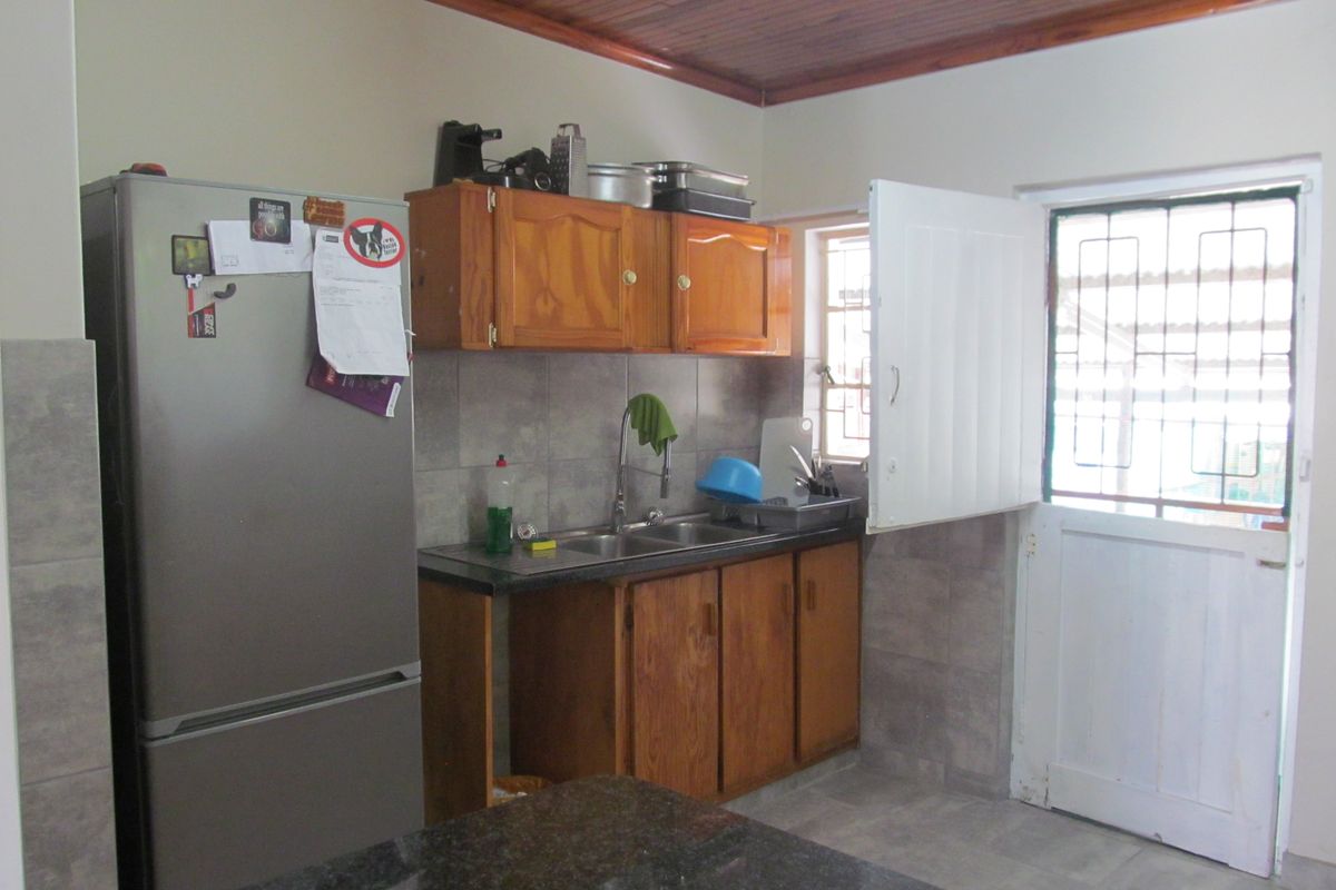 A functional kitchen featuring wooden cabinetry, tiled splashbacks, a double sink, and direct access to the exterior via a security-fitted door.