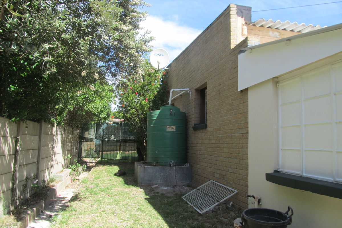 Side exterior view of the property featuring a brick facade, a water storage tank on a concrete plinth, and a fenced garden area.