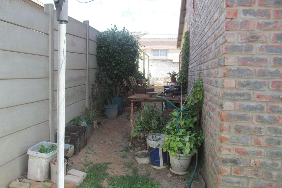 A narrow side yard area featuring a precast concrete boundary wall and exposed brick exterior wall, offering potential for landscaping or utility storage.
