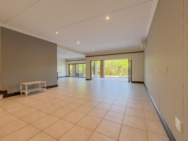 Spacious open-plan living area featuring neutral tiled flooring, recessed lighting, split-system air conditioning, and large sliding doors opening to an outdoor patio space.