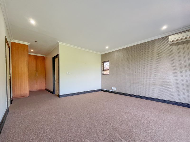 Spacious bedroom featuring built-in cupboards, carpeted flooring, an air conditioning unit, and a feature wall with textured wallpaper.