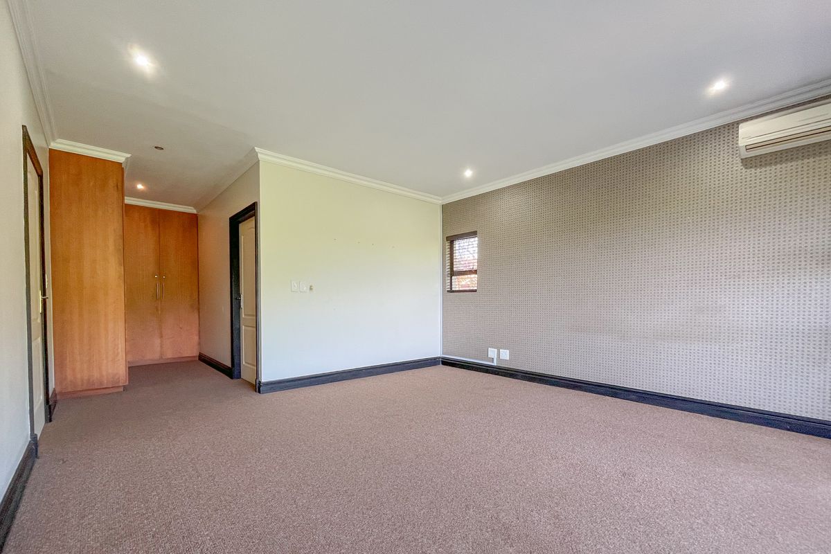 Spacious bedroom featuring built-in cupboards, carpeted flooring, an air conditioning unit, and a feature wall with textured wallpaper.