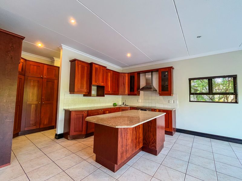 Spacious kitchen featuring warm-toned wooden cabinetry, granite countertops, a central island, and tiled flooring, offering a functional and well-maintained cooking space.