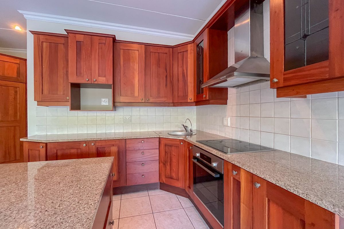A functional kitchen featuring warm-toned wooden cabinetry, granite countertops, a built-in oven, electric hob, and a stainless steel extractor fan.