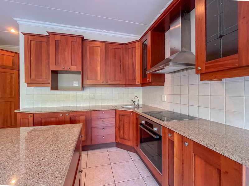 A functional kitchen featuring warm-toned wooden cabinetry, granite countertops, a built-in oven, electric hob, and a stainless steel extractor fan.