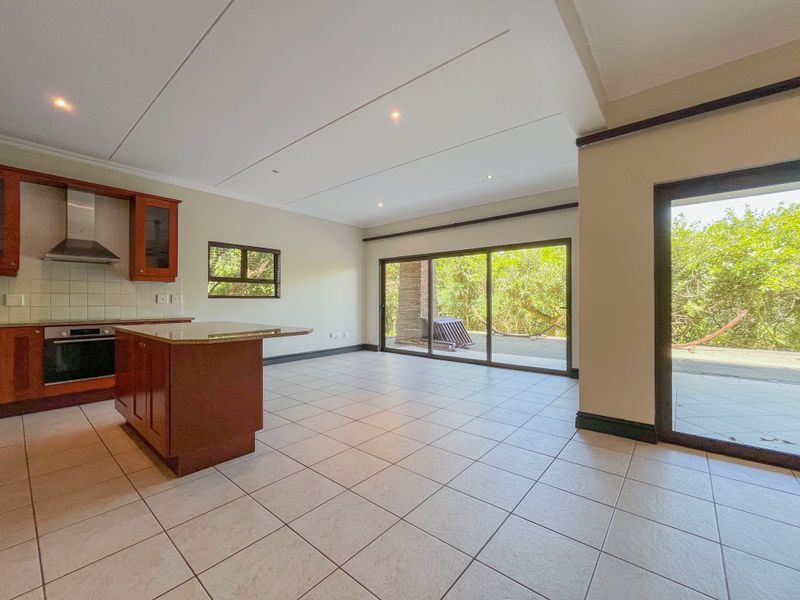 Spacious open-plan kitchen and living area featuring tiled floors, a central island, built-in oven, and large sliding doors leading to an outdoor deck.